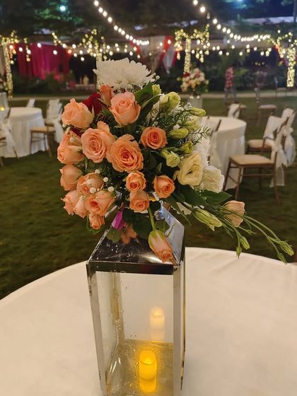 A simple yet beautiful pathway for a reception, with strings of fairy lights overhead and elegant table centerpieces featuring lanterns and fresh flowers.