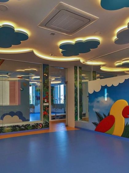 A room with a parrot-themed bookshelf and a sky-like ceiling with backlit clouds. The use of mirrors and glass walls creates a sense of openness and connection between different learning spaces.
