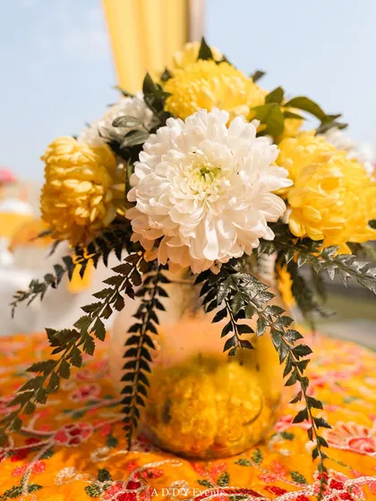 A beautiful centerpiece for the Haldi, with yellow and white chrysanthemums in a glass jar on a patterned tablecloth.
