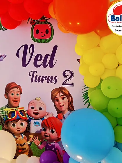 A close-up of a Cocomelon-themed backdrop, featuring the whole family and a colorful rainbow balloon garland.