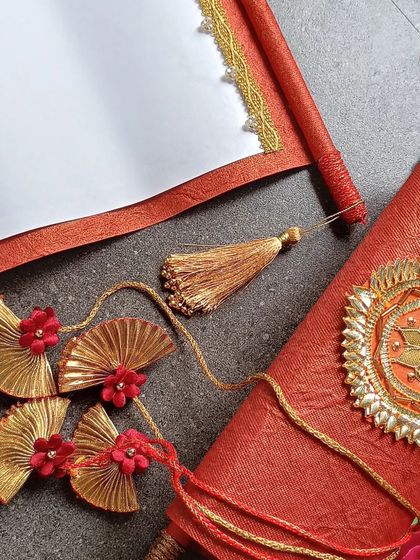 An open wedding scroll, showing the blank canvas ready for your invitation, alongside the intricate Gota-style embellishments and tassels.