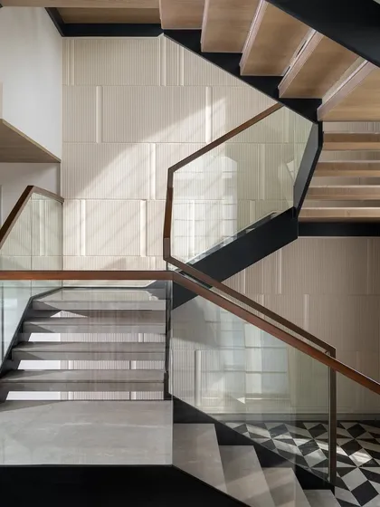 A staircase is more than just a connection between floors; it is the spine of the home. This sculptural piece combines the lightness of glass with the warmth of wood, set against fluted wall panels and geometric marble flooring. We design these transitional moments to be an experience of architectural beauty and grace.