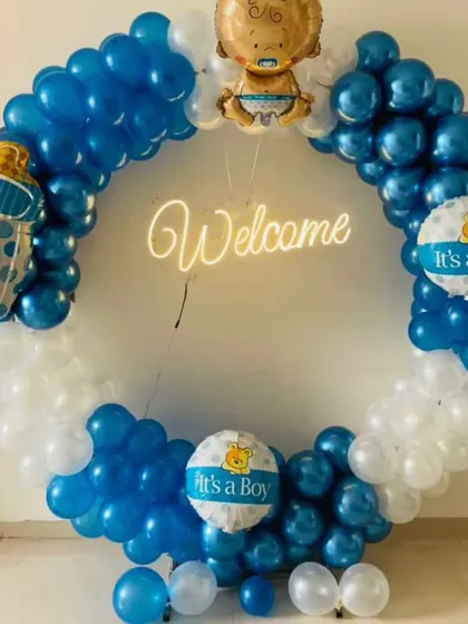 A bright and cheerful welcome for a baby boy. This full-circle balloon arch in blue and white features a 'Welcome' neon sign and several 'It's a Boy' themed foil balloons.