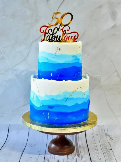 A cake to celebrate being "50 & Fabulous." This two-tier design features a beautiful blue ombre watercolor effect, accented with flecks of gold leaf for a touch of modern elegance.