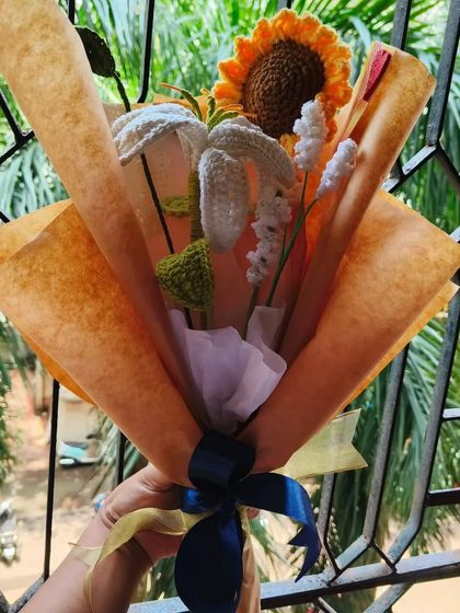 A beautiful custom bouquet featuring a sunflower and white lilies, wrapped in brown paper and tied with a blue and gold ribbon.