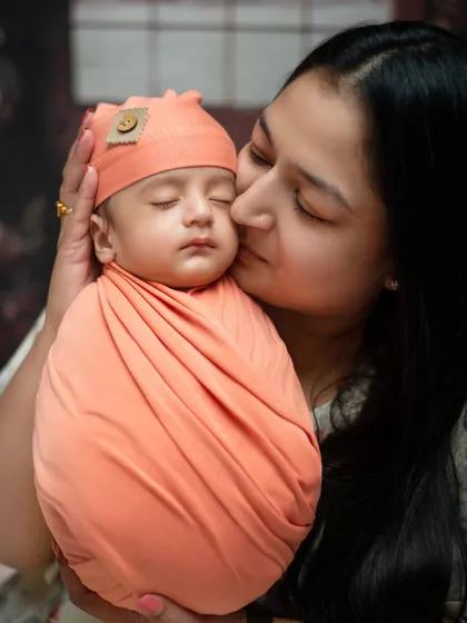 A mother’s gentle kiss for her sleeping newborn. Our specialized newborn sessions focus on creating these quiet, precious moments, using soft wraps and props to ensure your baby is safe and comfortable.
