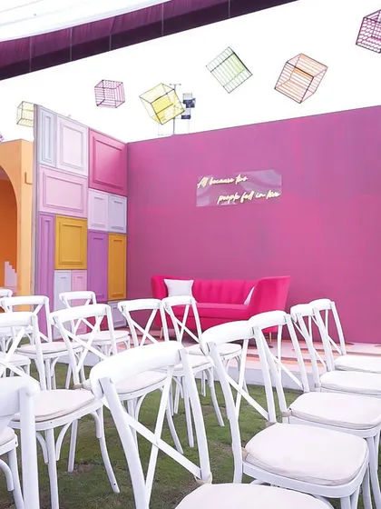 A lounge area with a vibrant magenta wall, a neon sign, and floating geometric cubes overhead, combining comfort with high-impact artistic design.