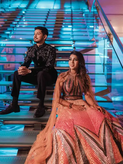 A stylish portrait of the couple seated on a modern, illuminated staircase, capturing a moment of cool composure amidst their vibrant reception.