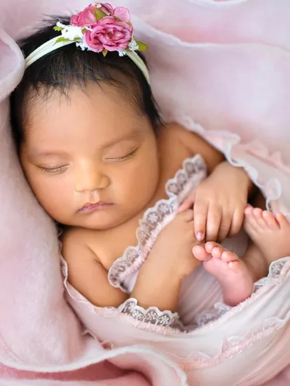 A detailed close-up of the baby nestled in the pink flower. You can see the delicate lace trim on her wrap and her perfectly peaceful expression.