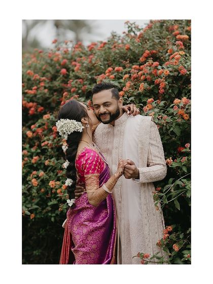 A sweet kiss amidst the flowers. This shot highlights the beautiful contrast and coordination between the bride's vibrant saree and the groom's softly colored, elegant sherwani.