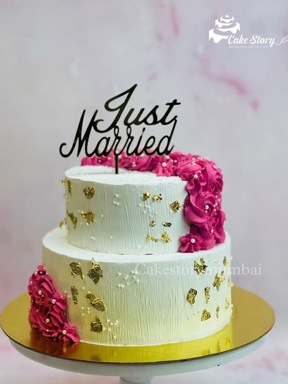 A 'Just Married' cake perfect for an intimate wedding celebration. The two-tier design features textured white frosting, gold leaf, and a cascade of vibrant pink icing.