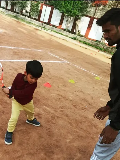 A coach guiding a young player through the backhand motion. Correcting the form at this age is crucial for long-term development.