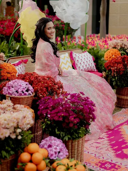 The bride poses in the lush floral setting, her pink and white lehenga beautifully complementing the colors of the decor.