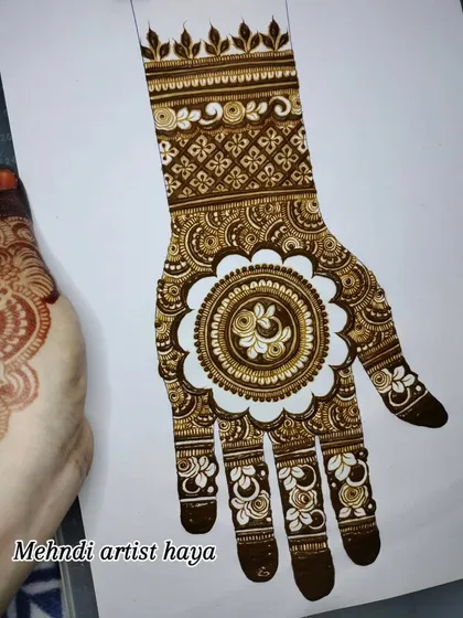 A close-up of a similar mandala design, showing the fine details within the central element and the delicate floral work on the fingers.