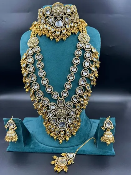This is one of our grandest bridal sets, perfect for making a statement. It features multiple layers of American diamonds and Kundan work, including a heavy choker, a three-layer rani haar, matching jhumkas, and a maang tikka. It gives you a luxurious designer look at an affordable rental price.