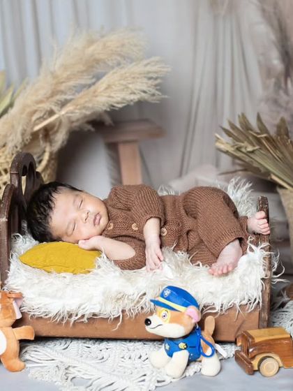 A peaceful newborn sleeping on a tiny wooden bed, with a gramophone and other vintage props nearby.