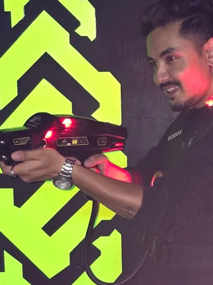A player smiles as he takes aim with his laser gun. The red lights on his vest and phaser show he's in the heat of the battle.