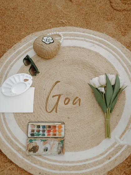 A flat-lay shot of the details from a Goa beach picnic. Featuring a watercolor set, flowers, and sunglasses, this image helps set the scene and highlights the thoughtful planning behind the shoot.