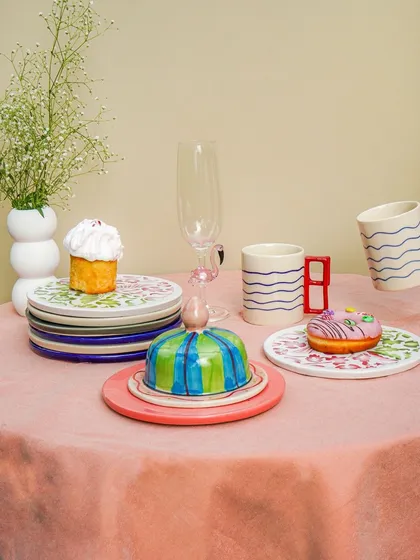 A full view of a styled table with unique, handmade crockery, flowers, and pastries, creating a whimsical scene.