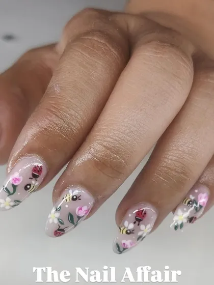 A detailed garden-themed manicure with hand-painted bees, ladybugs, and flowers on long, clear almond nails.