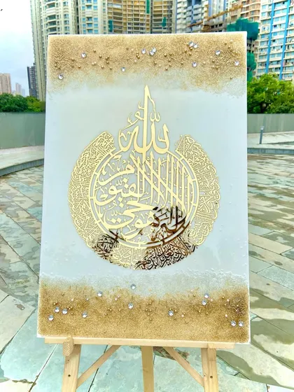 This stunning Ayat Ul Kursi resin art piece, set on an easel, embodies peace and protection. It features intricate golden calligraphy on a white and sand-colored background, blending Islamic symbolism with refined luxury.
