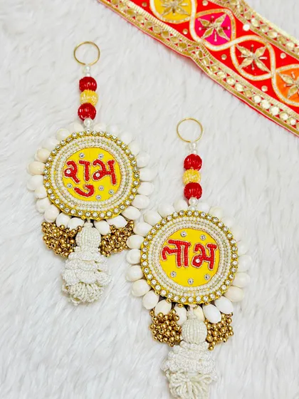 This Shubh Labh hanging is adorned with cowrie shells and golden beads. The bright yellow center makes the red lettering pop, creating a traditional and earthy look.