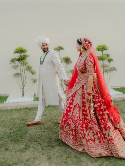 A full-length portrait of the couple walking hand-in-hand, their traditional red and white attire looking regal and elegant.