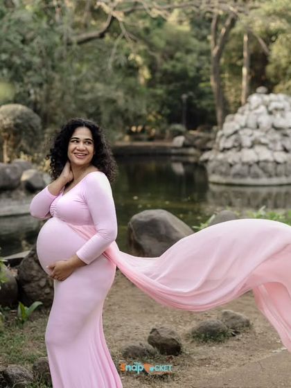 This mom-to-be looks like a princess in her pink gown, set against the beautiful backdrop of a park pond. The flowing train of the dress adds a touch of drama and elegance to this outdoor portrait.