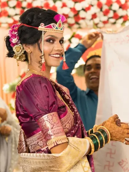 The bride's joyful glance over the Antarpat, a perfect candid moment that shows the excitement of a Maharashtrian wedding ceremony.