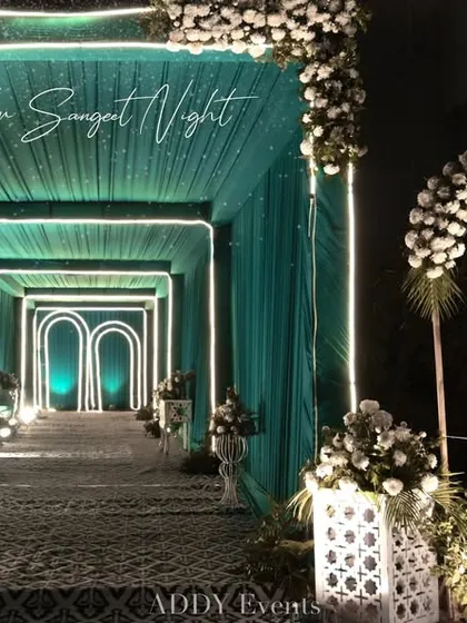 A stunning entrance tunnel designed with teal drapery and illuminated geometric arches. This modern and stylish walkway sets a sophisticated tone for guests as they arrive at a corporate cocktail party or gala.