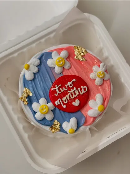 A cute two-month anniversary bento cake with smiley-face daisies and gold leaf accents.