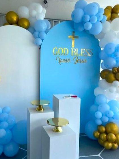 A First Holy Communion balloon decoration in blue, white, and gold. The setup uses modern arch backdrops and pedestals for a clean look.