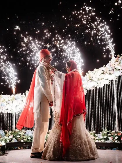 The grand Varmala exchange, complete with fireworks. This shot captures the scale and excitement of the ceremony, freezing a spectacular moment in time against the night sky.