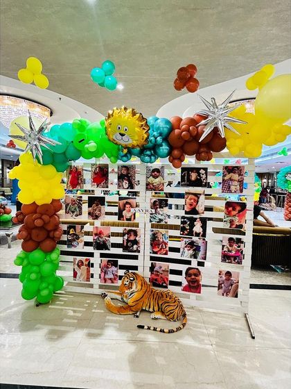 A creative photo memory wall for a jungle party, with a large tiger prop sitting in front, making for a great photo opportunity.