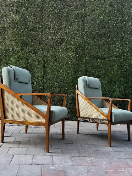 A pair of high-back lounge chairs with caned sides and an adjustable headrest for extra comfort. These chairs are built with a solid teak frame and upholstered in a durable sage green fabric, perfect for a reading nook or living room.