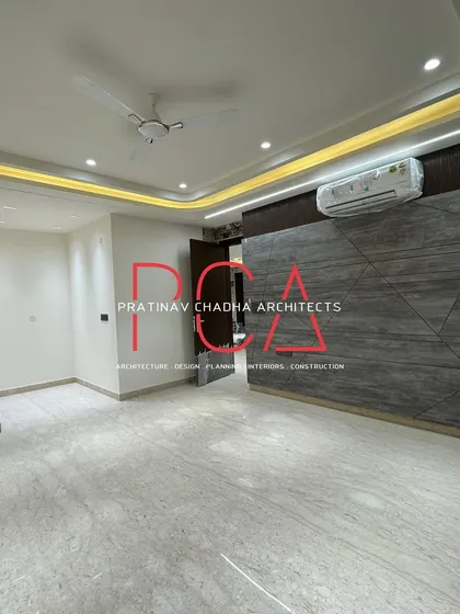 A final check of the living area in the Vasant Kunj luxury residence just before handover. The space features a geometric-paneled feature wall and a curved false ceiling with cove lighting, creating a modern and spacious feel.