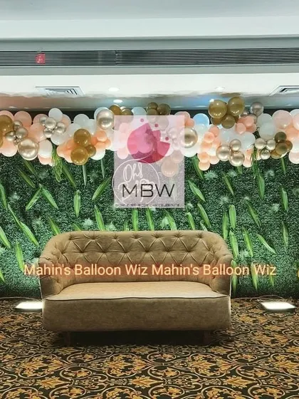 The main seating area for the modern baby shower, featuring a tufted sofa set against a greenery wall and framed by a matching balloon garland.