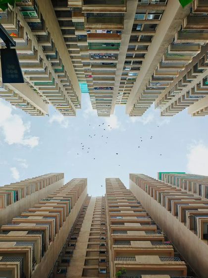 A worm's-eye view looking up at towering apartment buildings against a blue sky. This perspective creates a powerful sense of scale and urban density.