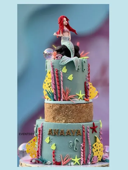 The beautiful mermaid-themed cake, featuring multiple tiers decorated with coral, shells, and an Ariel topper.