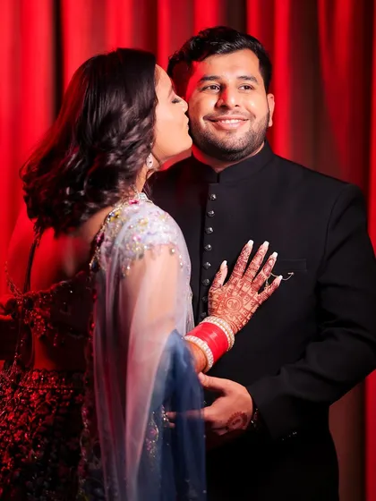 A playful and sweet moment from a celebration. The bride gives the groom a kiss on the cheek, leaving a lipstick mark. This candid shot is full of personality and captures the fun, romantic spirit of the couple's relationship.