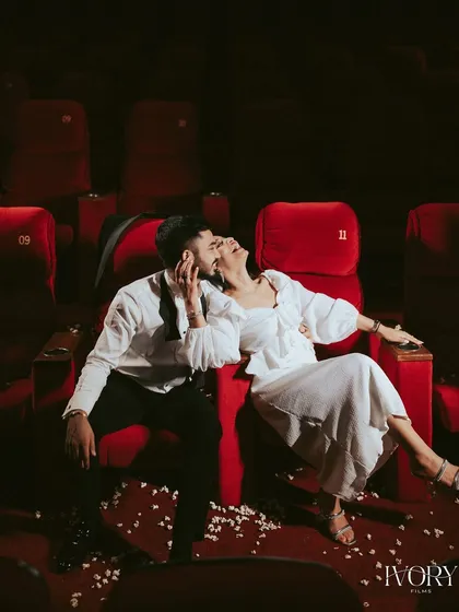 A moment of pure, unscripted joy during a unique pre-wedding shoot in an empty theatre. The dramatic red seats and scattered popcorn set the stage, but their genuine laughter is the real story here, showcasing a love that's playful and real.