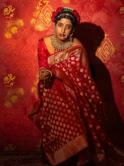 A powerful shot of Ketaki Narayan in a red Banarsi silk saree against a rich, patterned backdrop. This festive look is all about drama and traditional opulence.
