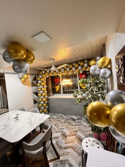 An elegant birthday surprise in a modern dining area. The window was framed with a gold and silver balloon arch and a neon sign, while balloon clusters throughout the room tied the whole celebration together.