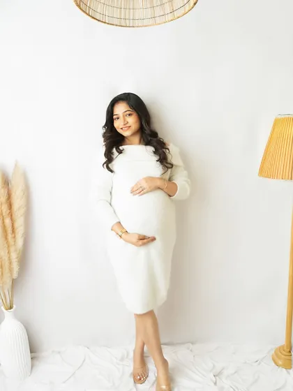 A smiling portrait in a simple white dress, taken in one of my studio's lifestyle corners. The warm lighting and props create a cozy, at-home feel.