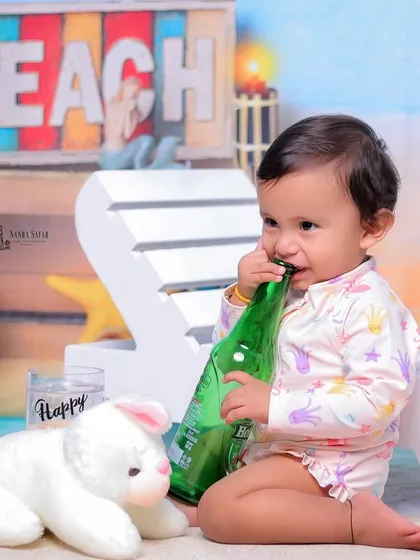It's always fun to see what babies will do with the props. This moment of a baby chewing on a bottle prop is a perfect example of their cute and unpredictable nature.