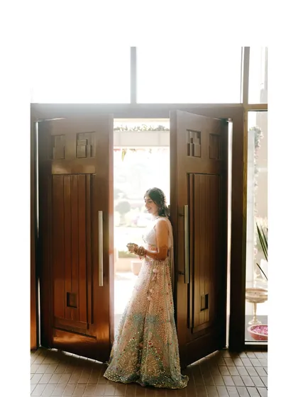 A grand entrance. The bride is framed by large wooden doors, creating a dramatic and beautiful portrait as she steps into her celebration.