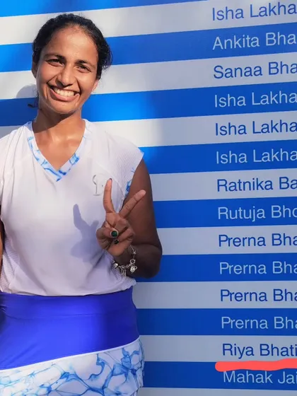 A smiling Riya Bhatia stands next to the honour board, with her name highlighted, after securing her spot in the semifinals of the Fenesta Open.