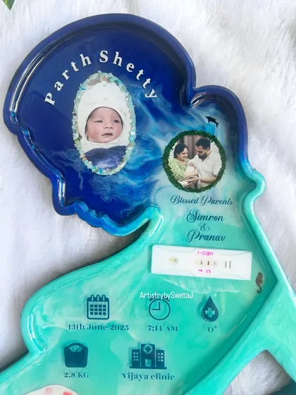The top portion of the motherhood frame, featuring the baby's name, photos, and the preserved pregnancy test. The deep blue and turquoise resin creates a beautiful ocean wave effect.