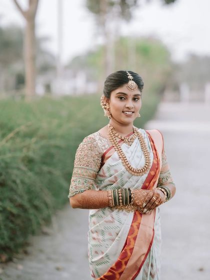 A beautiful outdoor bridal portrait. The bride's simple and elegant white saree and traditional jewelry are perfectly complemented by the natural surroundings.