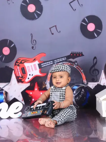 A smiling baby plays a toy keyboard in the middle of a rockstar-themed set. This shot captures the fun and interactive nature of my themed photoshoots.